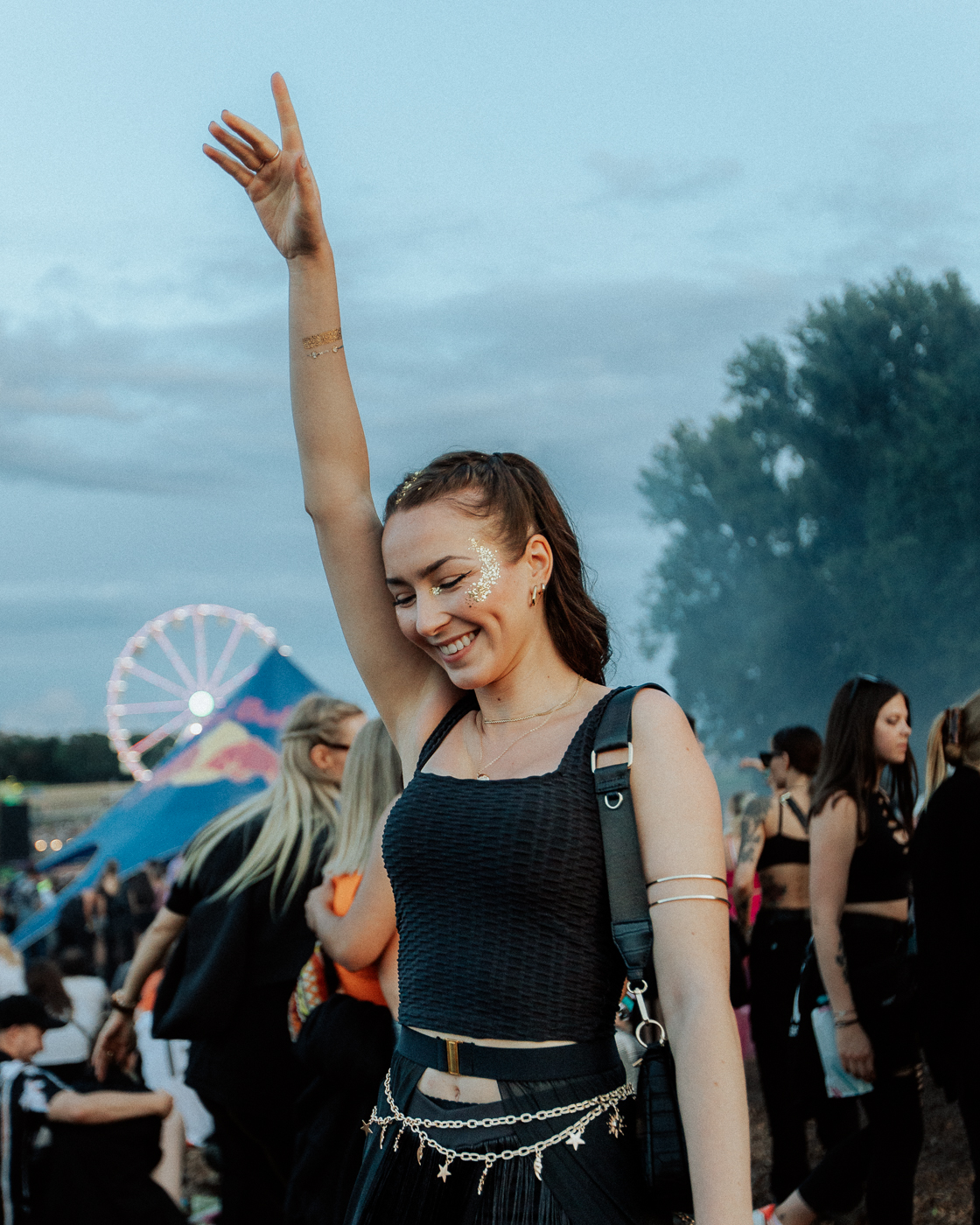 Eine Frau streckt ihren Arm in die Luft. Sie grinst. Der Himmel im Hintergrund ist blau, es sind viele Festivalbesucher des OpenBeatzs nahe Nürnberg zu sehen.