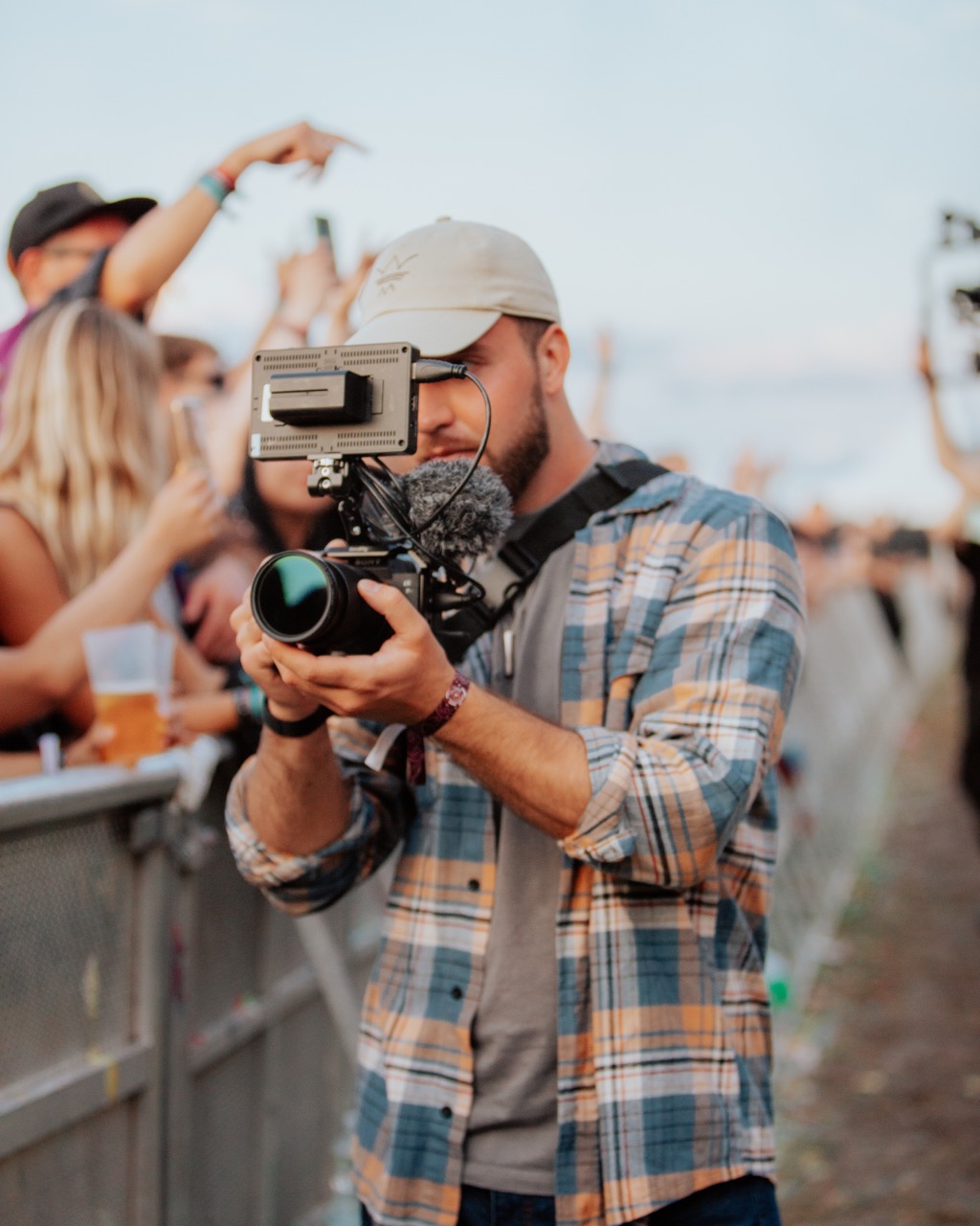 Ein Mitgleid unseres Teams filmt einen Act auf einem Festival. In der Hand hat er eine geriggte Kamera, mit Monitor. Das Bild ist schwarz weiß, im Hintergrund sind viele Menschen.